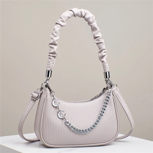 Detail of cream half-moon handbag with scrunchie handle and silver chain ornament
