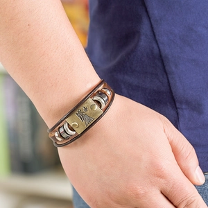 Close-up of a brown braided leather zodiac bracelet with a bronze plate on the wrist