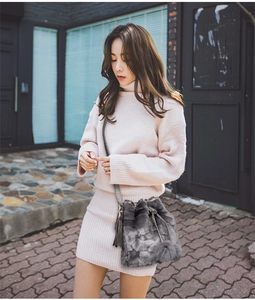 Gray faux fur bucket bag with plush pompom drawstring on a model in urban street setting