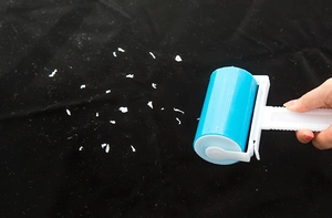 Washable lint roller removes white debris from black fabric surface efficiently
