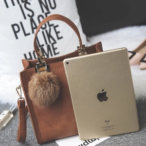 Sac bandoulière en similicuir marron mat avec pompon décoratif sur une couverture
