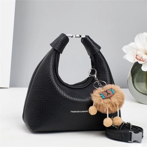 Close-up of black lychee leather crescent handbag with plush lion charm and silver hardware