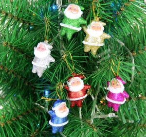 Close-up of six colorful glittery Santa Claus ornaments hanging on a Christmas tree branch