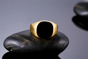 Macro detail of a classic masculine gold signet ring with black oil-drip inlay.