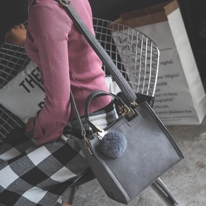 Detailed view of gray textured square handbag with plush pom-pom charm and golden hardware