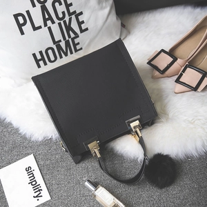 Detail of black matte handbag featuring gold hardware and a decorative plush ball charm