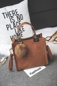 Brown matte frosted leather small square handbag with pompom charm on a soft rug