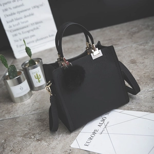Detail of black structured handbag with gold hardware and decorative pom-pom accessory