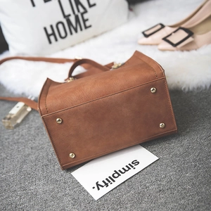 Brown frosted leather crossbody bag featuring metal feet studs and handle in home setting