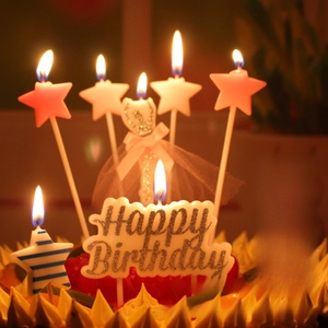 Star-shaped candles and Happy Birthday topper set with glitter on a lit cake