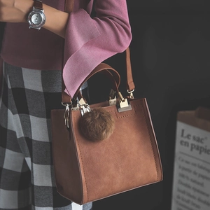 Detail of brown crossbody bag featuring gold hardware and a soft fur ball ornament