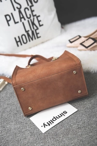 Detail view of the brown leather handbag base featuring four protective metal feet studs