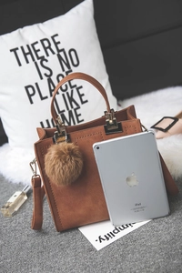 Brown frosted leather handbag with a plush fur ball charm in a cozy lifestyle setting
