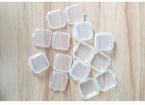 Multiple clear plastic square storage boxes with hinged lids on a light wooden table