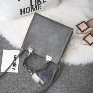 Chic gray matte square handbag with pompom charm and golden hardware on lifestyle background