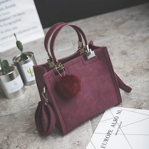 Close-up of wine red matte handbag with plush pom-pom charm in a lifestyle setting