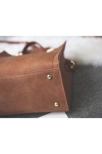 Detailed close-up of brown leather bag bottom featuring gold metal studs and fine stitching