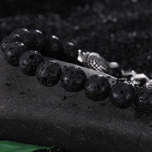 Handcrafted black volcanic lava stone bead bracelet with silver charm on dark rocks