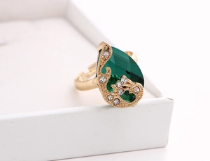 Macro shot of gold-plated ring with pear-shaped green crystal and white diamond accents