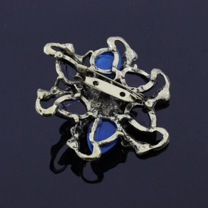 Macro shot of bronze flower brooch back with blue resin gemstones on black reflective surface