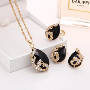 Detailed macro view of gold-plated teardrop necklace, ring, and earrings set with black crystal