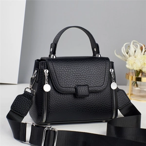 Detail of black pebbled leather handbag featuring silver zippers and adjustable wide strap