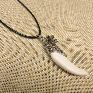 Detailed close-up of a wolf tooth resin pendant with an antique silver dragon clasp and black cord
