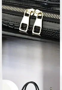 Detail der goldenen Doppelreißverschlüsse und Krokodil-Prägung auf der schwarzen Handtasche