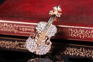 Dettaglio spilla a violino dorata con strass bianchi su scatola rossa vintage