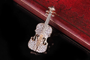 Dettaglio di una spilla a forma di violino dorato con strass su una scatola vintage