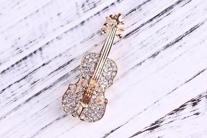 Dettaglio di una spilla a forma di violino dorata con strass di cristallo scintillanti