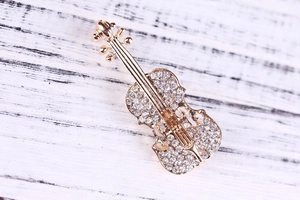 Dettaglio spilla a violino in lega dorata con strass bianchi scintillanti su base metallica