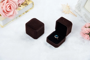 Detailansicht von offener und geschlossener brauner Samt-Ringbox mit Schmuck auf Stoff