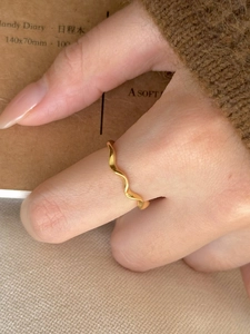 Close-up of a minimalist golden wavy ring on a finger with a warm aesthetic background