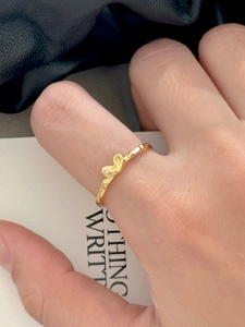 Detail of a wavy gold ring with a sparkling solitaire zircon on a model's finger