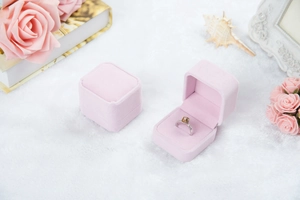 Rosa Samt-Ringbox offen präsentiert mit Diamantring auf weißem Plüschhintergrund