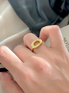 Macro shot of minimalist gold oval hollow ring worn on finger with soft texture background