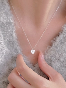 Detail view of S925 silver heart necklace with bow engraving on grey plush sweater