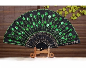 Close-up of black folding fan with green sequins peacock pattern on wooden stand