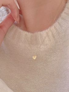 Close-up of golden heart pendant with bow relief and bead edge on minimalist chain