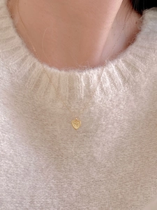 Detail of gold heart necklace with milgrain edge worn over a soft cream knit sweater