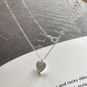 Detailed macro view of heart pendant with bow relief on polished silver chain
