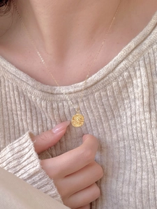 Detail view of a round gold pendant on a gold chain, styled on a beige knitted sweater