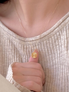 Detail of a gold-tone sunburst pendant necklace worn over a beige knitted sweater