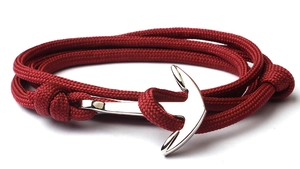 Detail of red braided rope bracelet featuring a polished silver metal anchor clasp