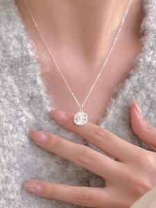 Detail of 925 sterling silver necklace with textured round pendant worn on a soft sweater
