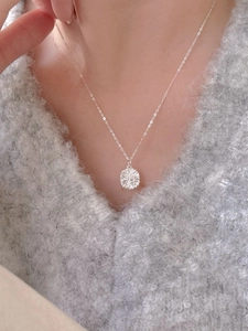 Close-up of a silver geometric textured round pendant necklace worn on a grey sweater