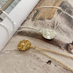 Detailed close-up of gold and silver woven pendant necklaces on a magazine
