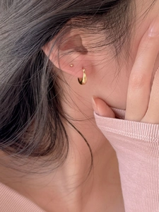 Gros plan de boucles d'oreilles créoles dorées en goutte et puces portées par un mannequin
