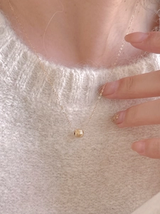 Detailed view of a gold S925 sterling silver ball necklace worn on a white knit sweater